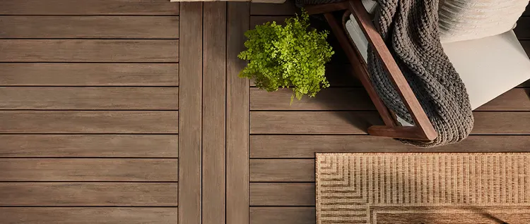 Aerial view of a medium brown deck with an armchair, rug, and potted plant on it.