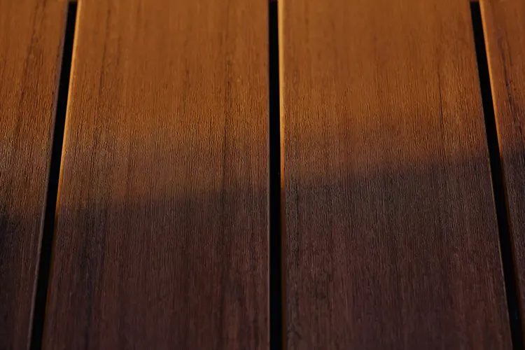 Close-up of four vertical Advanced PVC planks with warm sunlight creating a gradient of orange and brown tones. The wood-like texture adds a cozy, natural feel.
