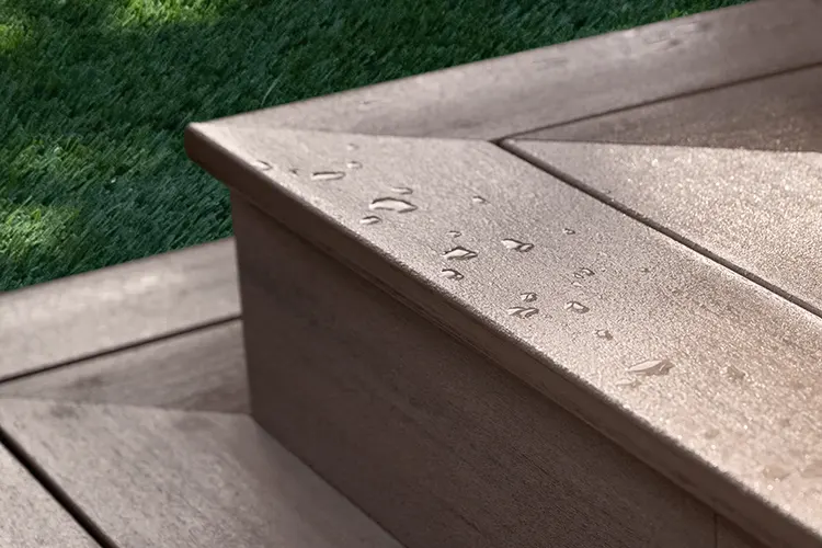 Close-up of a wet composite deck corner with water droplets, set against a green grass lawn, conveying a fresh, serene morning after rain.