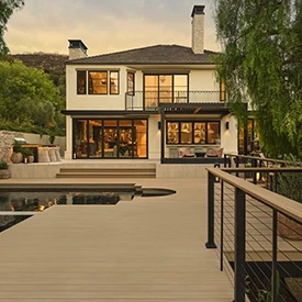 Backside of home at sunset with expansive light tan deck and an in ground pool