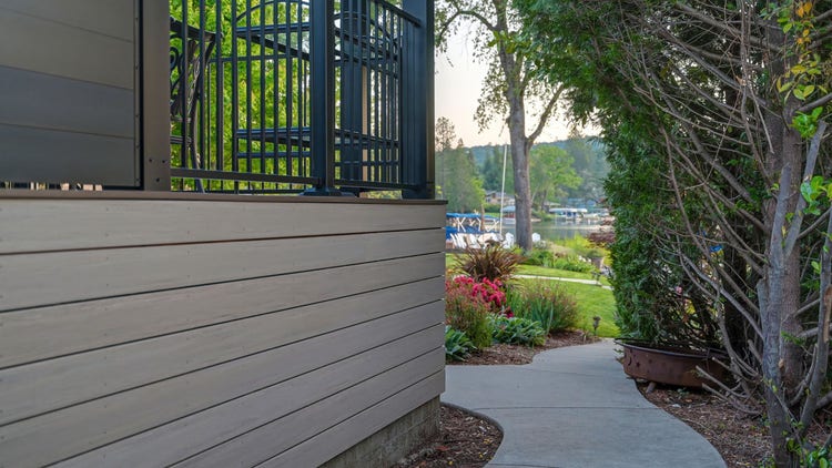 Matte-black aluminum privacy wall on an AZEK Landmark Collection deck in French White Oak with cladding, photographed at golden hour on a lakefront home on Lake of the Pines in Auburn, California. Built by Stone Ridge Decking — custom decks across Northern California, serving Granite Bay, Folsom, Roseville, Lake Tahoe, Auburn, Sacramento, and Grass Valley. https://stoneridgedecking.com
