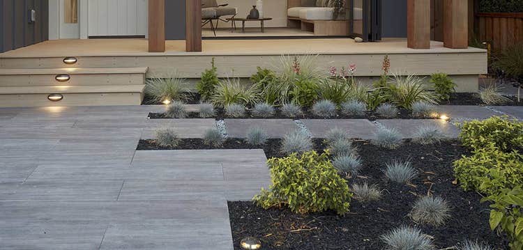 A path up to a front porch is surrounded by low-lying landscaping with ground-level landscaping lights throughout.