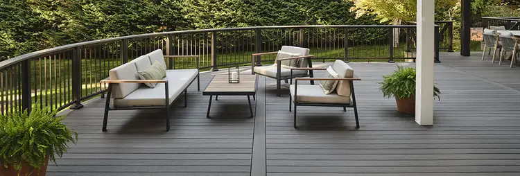 Photo of a gray deck with curved edge and railing in a secluded backyard surrounded by evergreen trees.