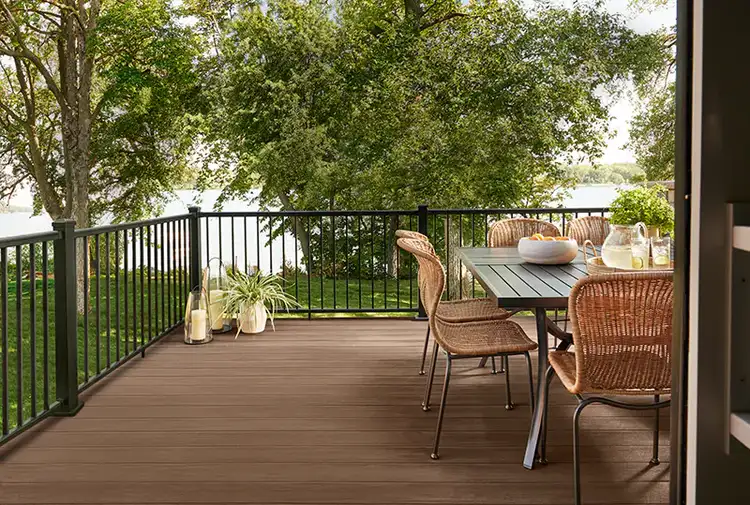 TimberTech deck in brown with black railing in a secluded backyard with a lake in the background. The scene is from the viewpoint of the back door of the home which leads to the deck.