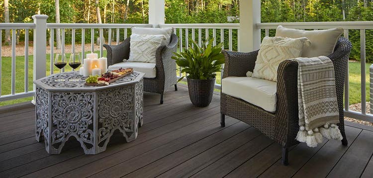 Two outdoor armchairs with upholstered cushions feature plump throw pillows and a tasseled blanket.