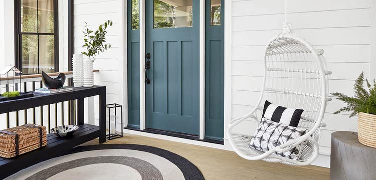 A suspended swing with pillows hangs by a front door with a narrow table across from it.