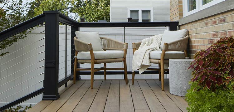 Cable infills on a black railing show a neighboring home and fence behind deck furniture.