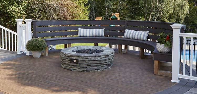 A built-in bench follows the curve of a deck’s perimeter with a fire pit in the center and railing on each side.