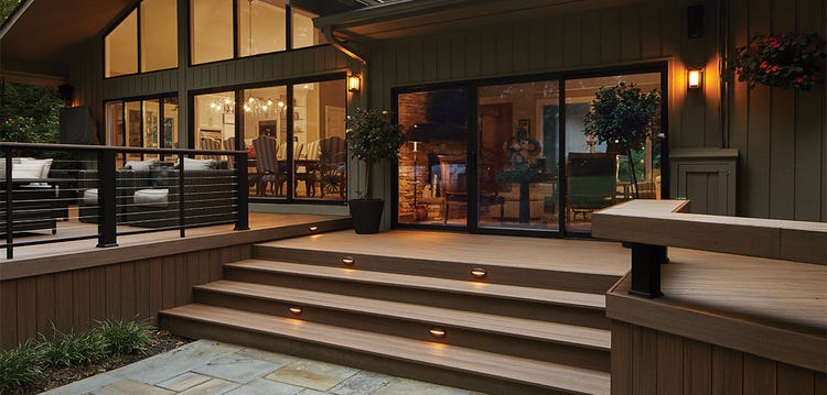 Wide deck steps lead to multiple deck levels and a large glass door.