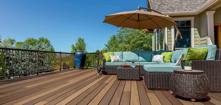 A brown outdoor sectional with light blue upholstery features lime green throw pillows, all on a deck with multi-colored decking boards.