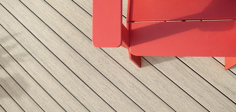 An overview close-up image of a beige composite deck includes the corner of a red outdoor chair.