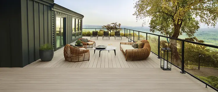 TimberTech Advanced PVC Vintage Collection decking in Coastline frames a modern outdoor space with black Impression Rail Express railing, glass infill, lounge seating, and a wooded view.