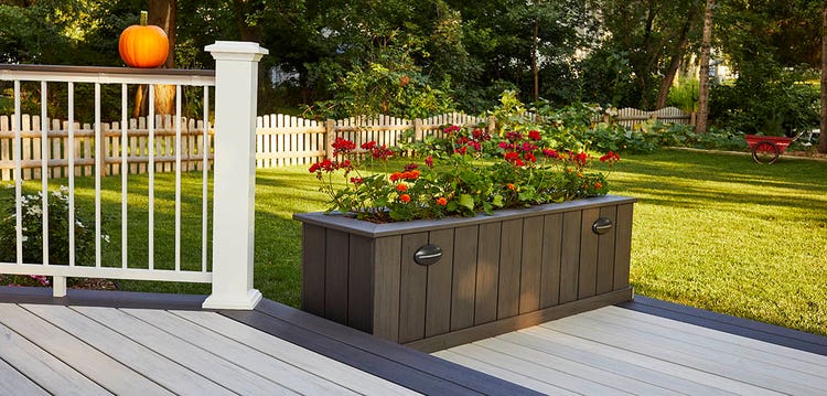 Red flowers bloom from the top of a custom raised planter installed on a lower deck level.
