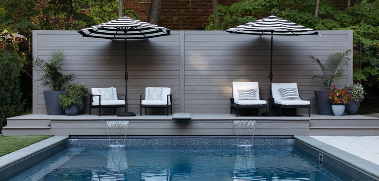 A poolside deck with umbrella-covered seating features waterfall spouts feeding into the pool.