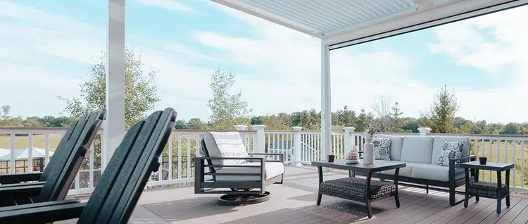 Light gray deck with multiple seating areas is partially shaded from the sun as it sits underneath a pergola