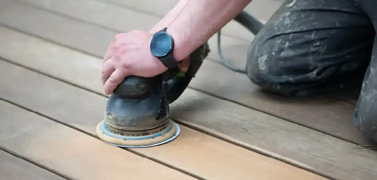 A random orbital sander removes a thin layer of a wood deck.