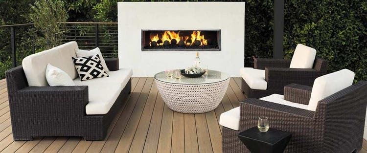A built-in outdoor fire place is lit on a medium brown deck