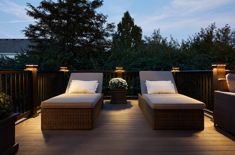 A deck at night with built-in lights surrounding two outdoor chaise loungers.