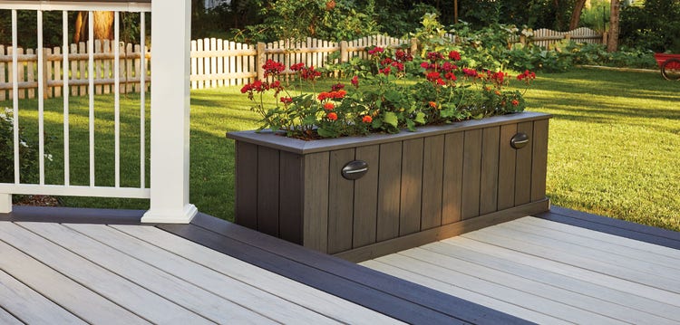 A built-in planter box lines the edge of a small deck platform and has red flowers blooming from the top.