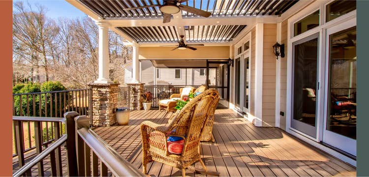 A sunny deck with woven furniture looks over the yard with a pergola and open louvers installed above.