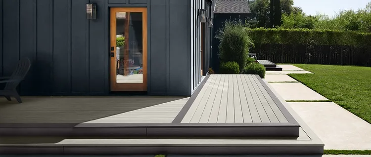 A two-tone deck with stairs off the back of a house features light grey deck boards and dark brown decking in a picture-framed deck pattern.