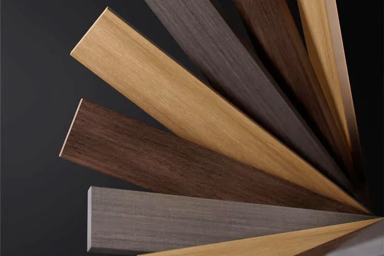 A fan-like array of composite deck planks in various shades from light brown to dark, set against a dark background. The composition evokes elegance and simplicity.