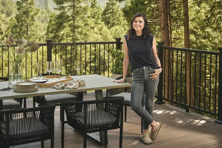 Tiffani leans on her outdoor dining table and smiles on her new deck