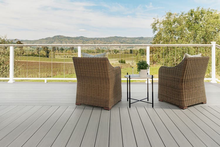 A patio, facing the mountains with lush greenery and vineyards, decorated with with wicker chairs and a short round table with a green fern plant.