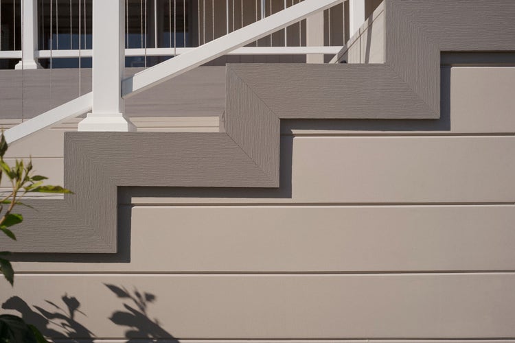 A detailed view of the white stair rail connecting to the home. The stairs are decorated with gray trim boards and brown decking.