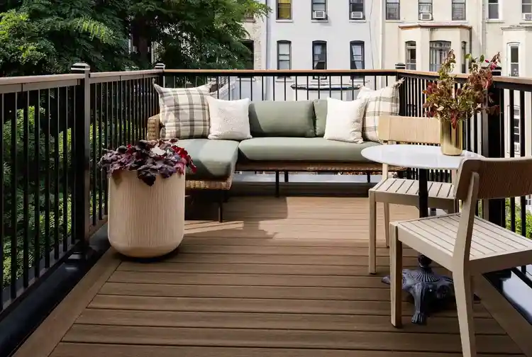 The new Brooklyn brownstone rooftop deck with a couch, two chairs and table. It is trimmed with Aluminum Framing in Classic Black. The light brown decking is English Walnut from the Vintage Collection. The soft glow of the sun illuminates the light pale green couch cushions.