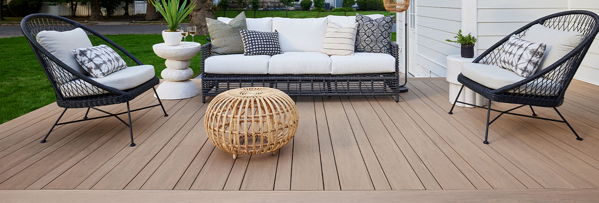 A deck with a pinstripe pattern and picture frame border design features a white couch and rattan table.