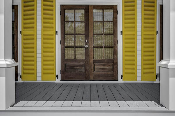Deck over concrete patio featuring double front door and yellow accents on a porch