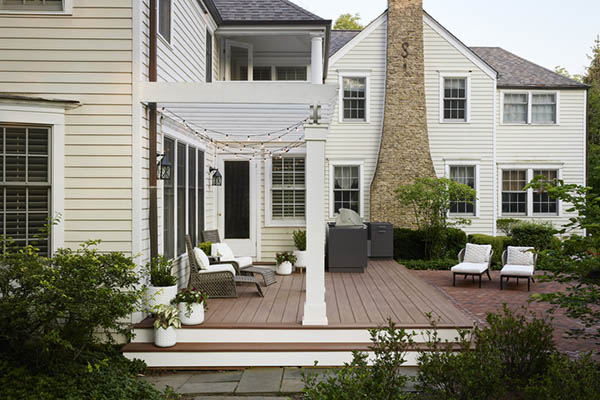 Deck over concrete patio featuring multi-level home with cobblestone chimney in furnished backyard deck