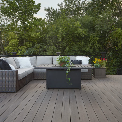 Richly hued composite deck with L-shaped couch and trees beyond the deck