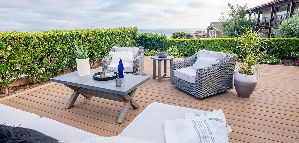 Deck surrounded by green hedge plants with a table and seating in the middle.