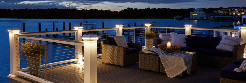 A sunset view of a lakeside patio with post cap lights illuminating the space.