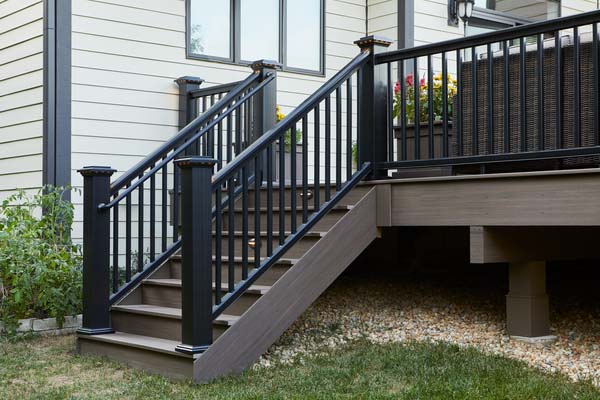 A black composite railing on a richly hued composite deck with a set of stairs leading to a lawn