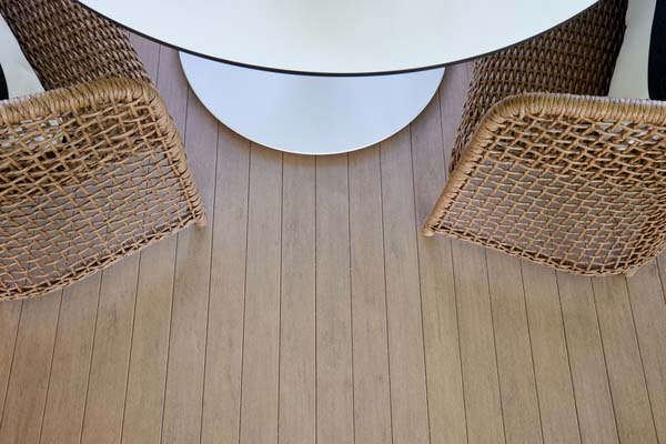 A close-up image of warm Weathered Teak TimberTech Porch boards with wicker chairs just out of view