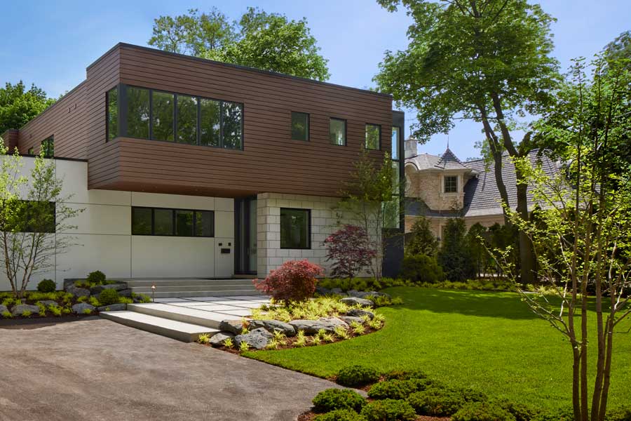 Modern, boxy home with a neatly manicured front lawn and shrubs