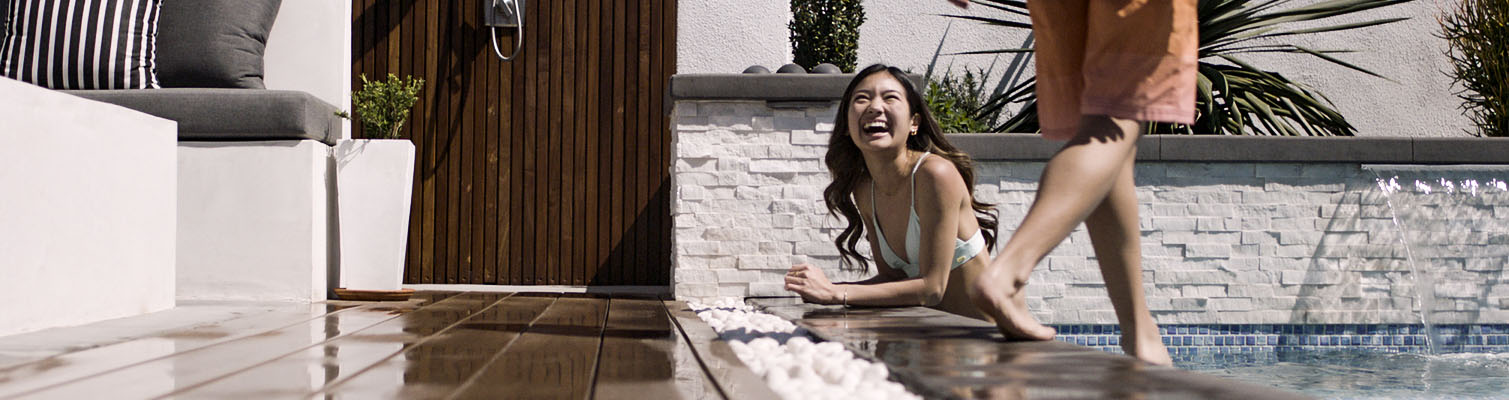 A customer success story homeowner leans over the side of a pool smiling next to TimberTech Deck