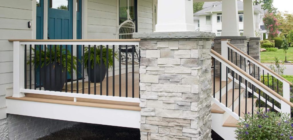 A craftsman-style home’s front porch showcases stone pillars with white railing, black vertical infill, and a light brown composite deck. 