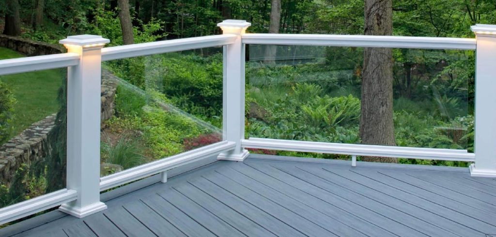 Glass infills in white railing with lighted post caps show a clear view of the woods and landscape beyond the deck. 