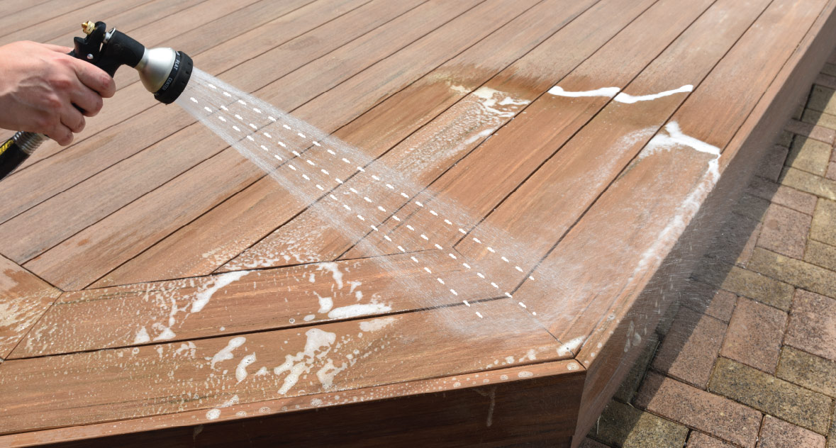 Someone rinsing soap and residue off the deck using a garden hose sprayer.