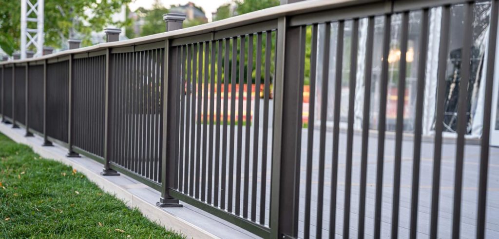 Black railing with vertical infills mimicks a wrought iron look and lines the edge of a composite deck. 