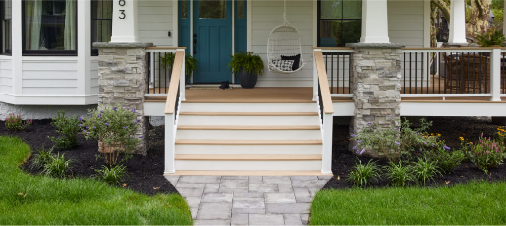 A craftsman-style home’s front patio is lined with flowerbeds and fresh mulch extends under the deck