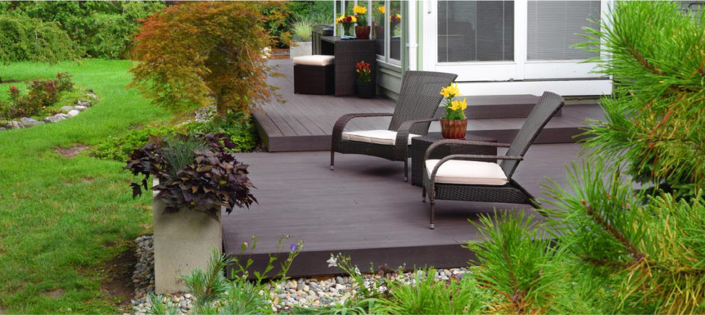 A low-lying deck with patio furniture has several levels and is surrounded by landscaping with a gravel perimeter