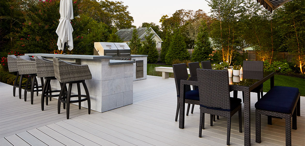 An outdoor gray kitchen and grill with dining table and bar seating.