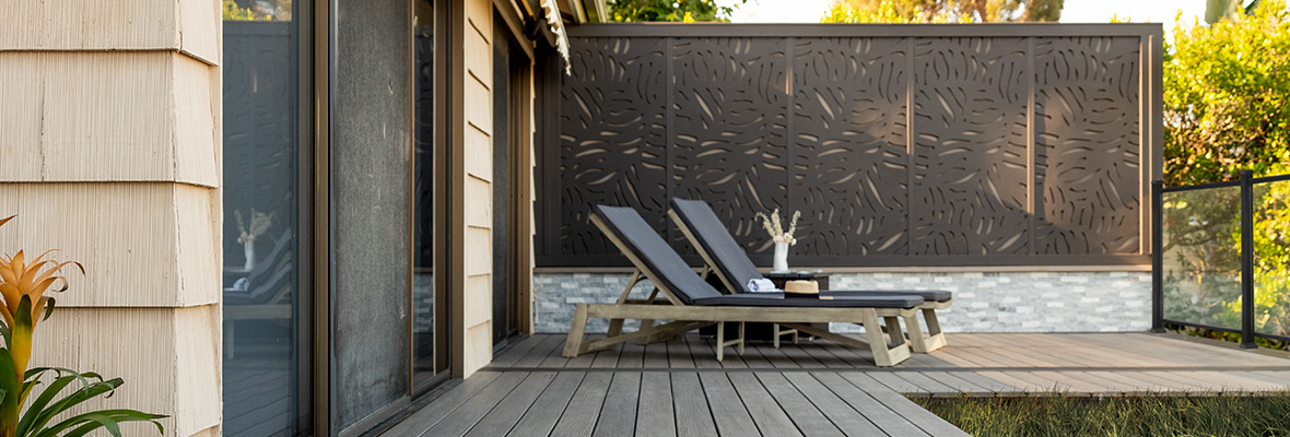 Two outdoor lounge chairs sit on a deck facing the yard with a decorative fence for privacy behind them.