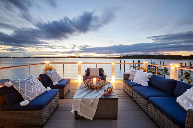 Nighttime shot of a deck on the water with blue couches and a coffee table