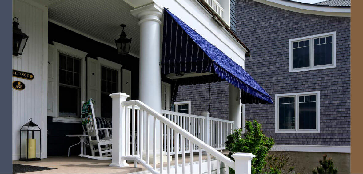 A front porch with white railing showcases a blue and white pinstripe fabric awning hanging between porch posts.